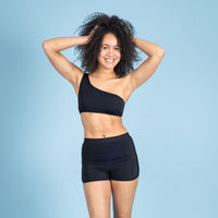 Vooraanzicht van de zwarte ZAYA menstruatiezwemboxershort van Moi et Marie met korte pijpjes en een sportieve pasvorm, gecombineerd met een zwarte zwemtop.